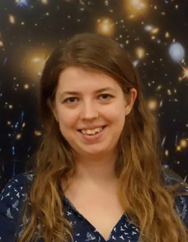 Smiling young woman with long brown hair wearing a dark blue shirt with white spots.
