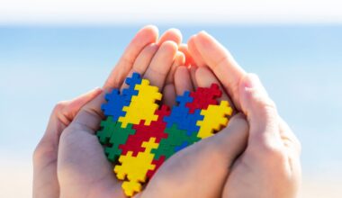 Child and adult hands holding colorful heart with blue background outdoors.
