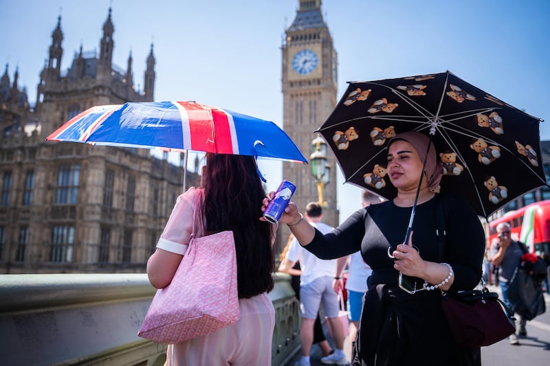 Tourists shelter from the sun beneath umbrellas during the hot weather on Westminster Bridge, central London. Photograph: James Manning/PA Wire
