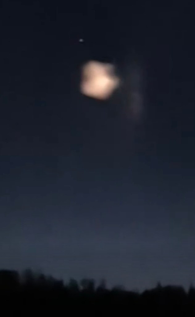 Bright, rectangular UFO with a faint light source above it, against a dark blue night sky and silhouetted trees.