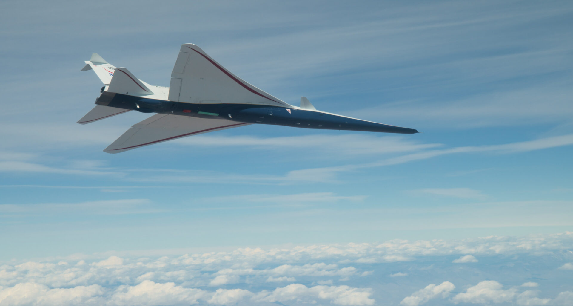 NASA's X-59 supersonic jet with blue hull and white wing and tail is seen from below as it flies among clouds.
