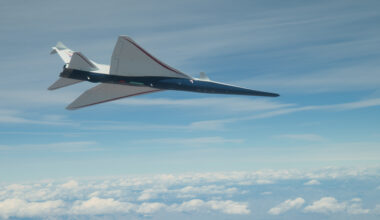 NASA's X-59 supersonic jet with blue hull and white wing and tail is seen from below as it flies among clouds.