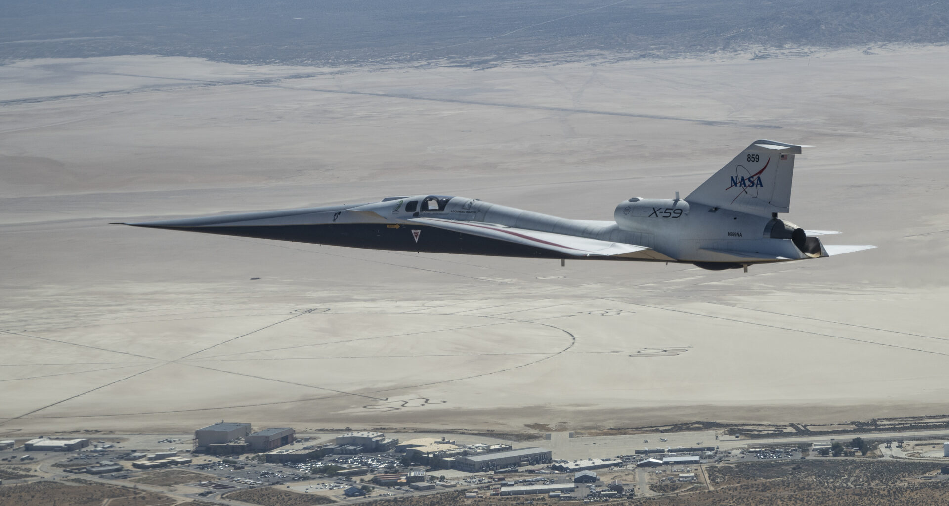 NASA’s X-59 quiet supersonic research aircraft flies above NASA’s Armstrong Flight Research Center in Edwards, California. The plane has a distinctive shape, with a very long, sharp nose.