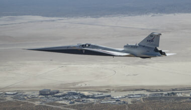 NASA’s X-59 quiet supersonic research aircraft flies above NASA’s Armstrong Flight Research Center in Edwards, California. The plane has a distinctive shape, with a very long, sharp nose.