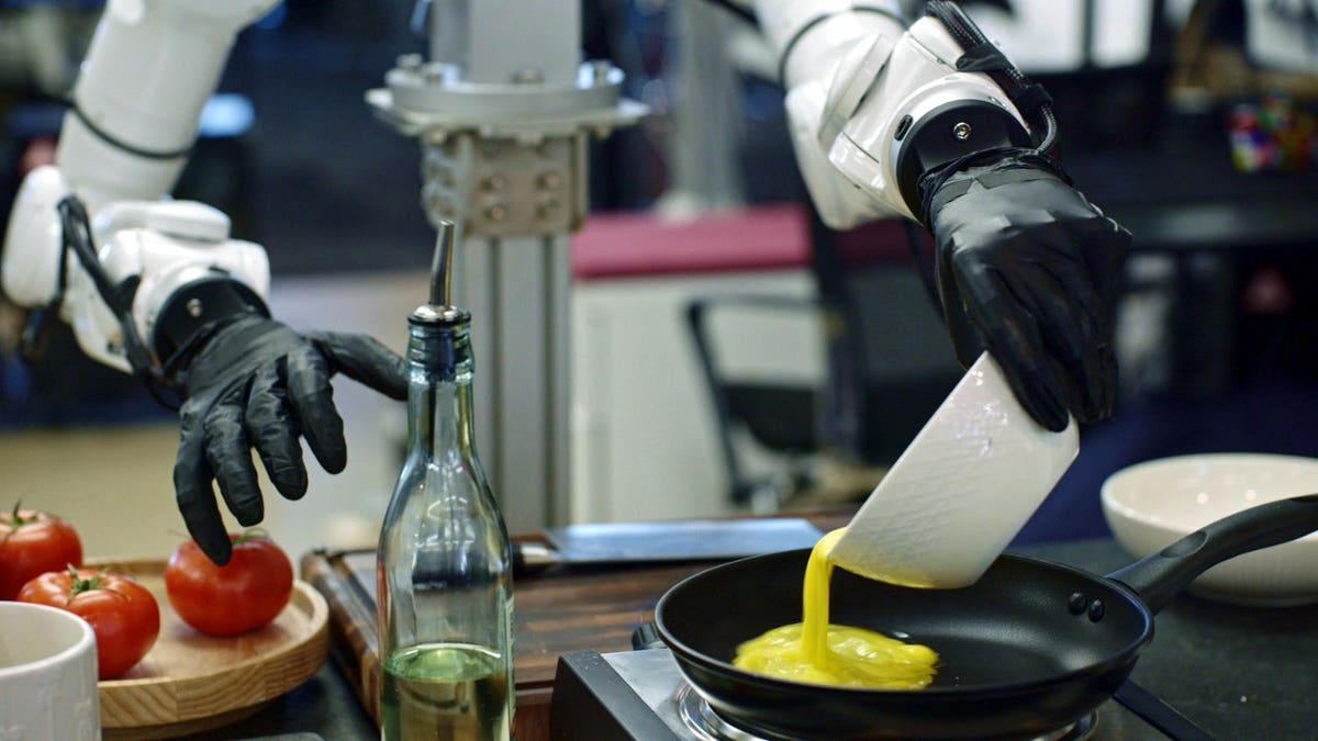 A robot pours eggs into a pan.