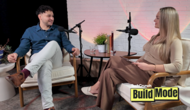 Two people seated in armchairs during a podcast interview, speaking into microphones across a small table with water glasses and a plant, with a “TechCrunch Build Mode” logo overlay in the corner.