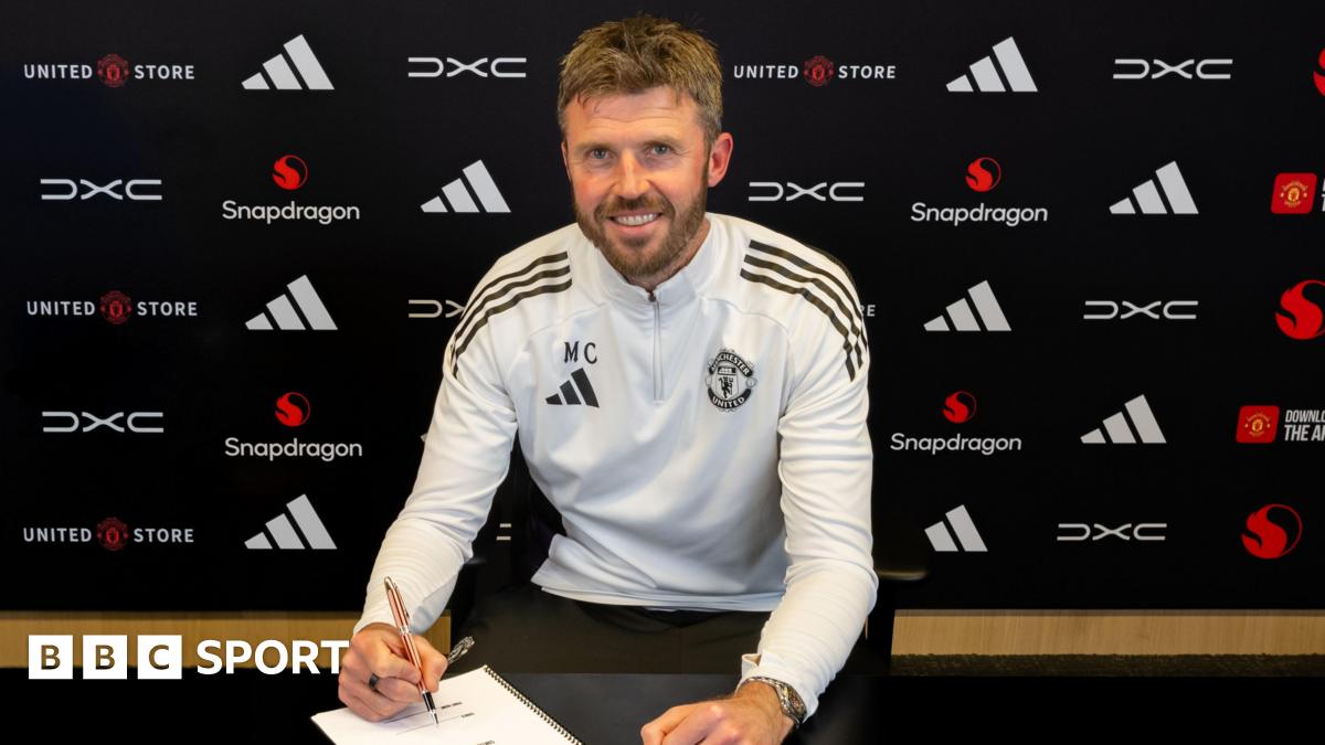 Michael Carrick sat down in Manchester United training kit, posing holding a pen over a contract document