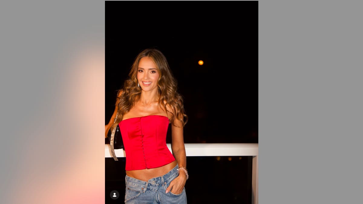 Jessica Alba posing in a red top and jeans.