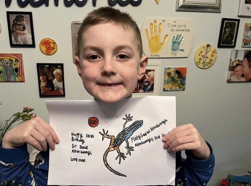 Max Evans-Browning, the 6-Year-Old superfan of David Attenborough, holding up his 100th animal drawing in celebration of Attenborough's 100th birthday