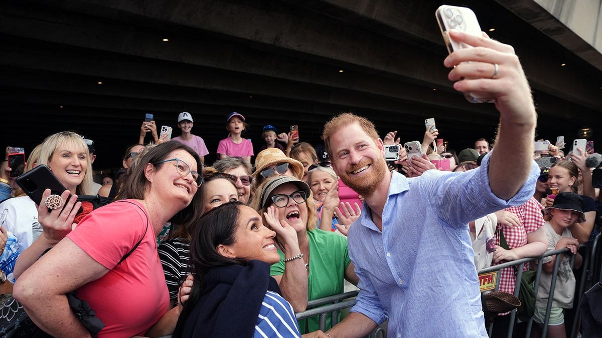 Prince Harry and Meghan Markle taking a selfie with well-wishers at a sailing event in Sydney Harbour