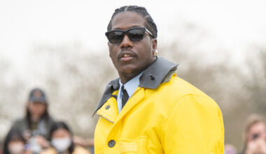 Lil Yachty in a yellow jacket and dark pants holds a blue bag, with a crowd in the background.