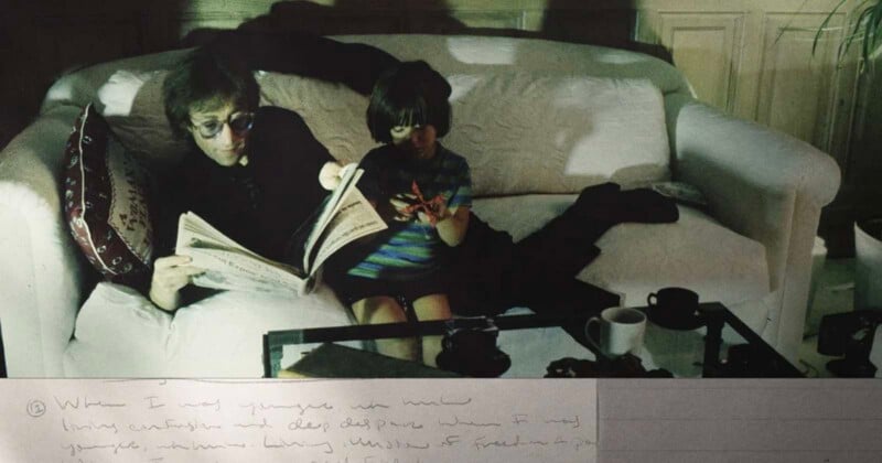 A man wearing sunglasses reads a newspaper on a white couch beside a young child holding up one hand. They are lit by greenish light, with coffee cups and papers on the table in front of them. Handwritten notes are partially visible at the bottom.