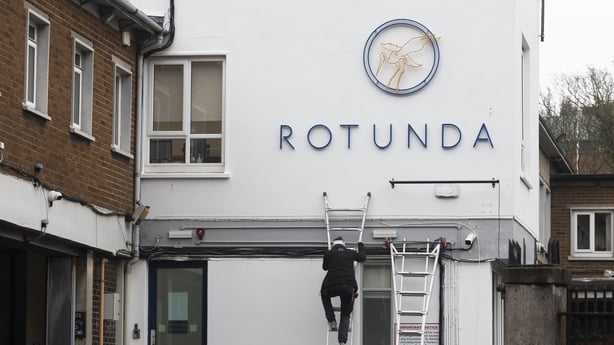 A man climbs a ladder beside a sign reading 'Rotunda' on a building on the hospital's campus