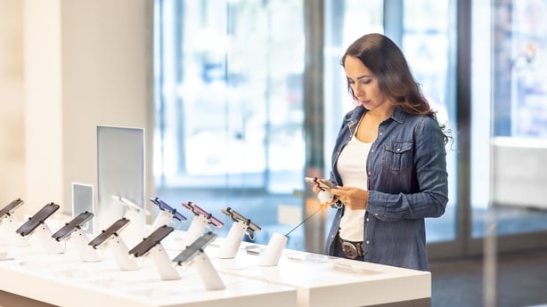A pretty brunette is trying out a new smartphone in a phone operator's store. She is getting to know the new model.