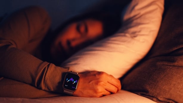 Young woman using healthcare app on smartwatch to improve sleep while sleeping in bed. Healthcare and technology.