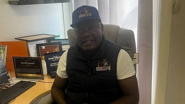 Jahswill Emmanuel, who works in Belfast, is sitting on a chair in an office