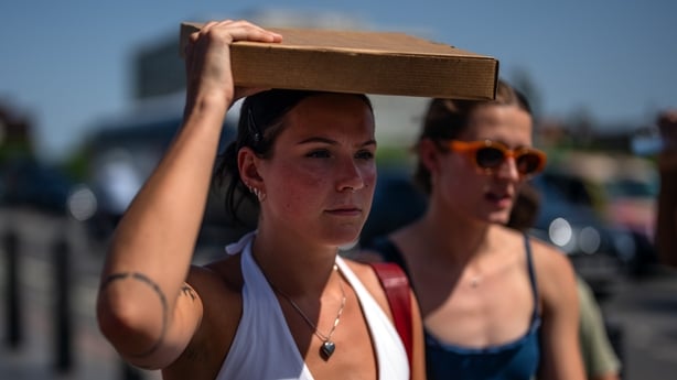 A woman uses a pizza box to shield her face from the sun as she walks through central London