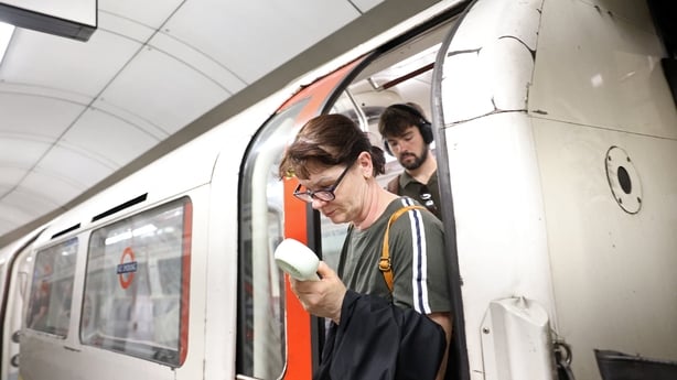 A commuter uses a fan in an attempt to cool down as she exits a London Underground tube carriage