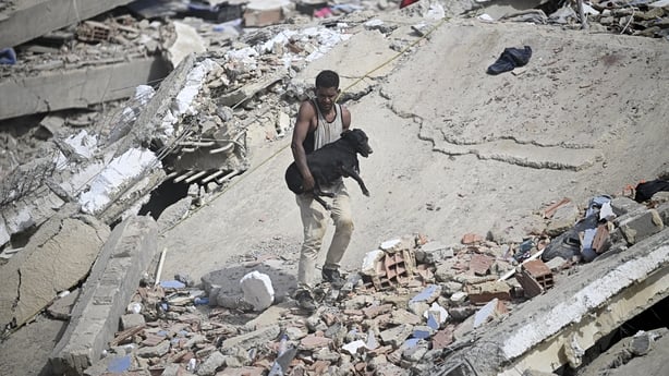 A volunteer carries a rescued dog across the rubble of a collapsed building following twin earthquakes in Caraballeda, La Guaira
