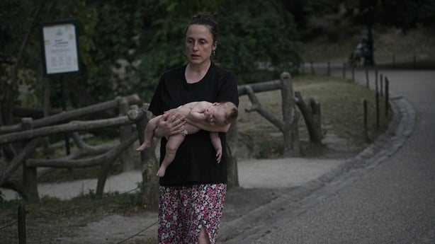 A woman is seen carrying a baby late in the evening in a park