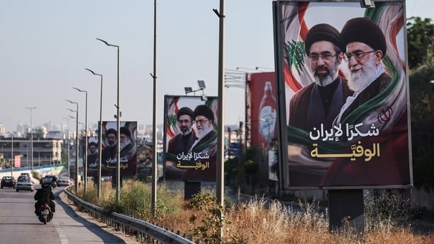 Cars and motorbikes drive past billboards showing Iran's new Supreme Leader Ayatollah Mojtaba Khamenei and his late father Ali Khamenei.