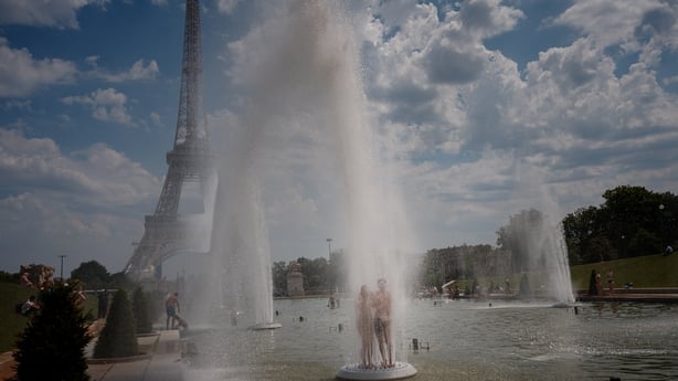 A couple cools off in the Trocadero Fountain with the Eiffel Tower on the background during a heatwave in Paris
