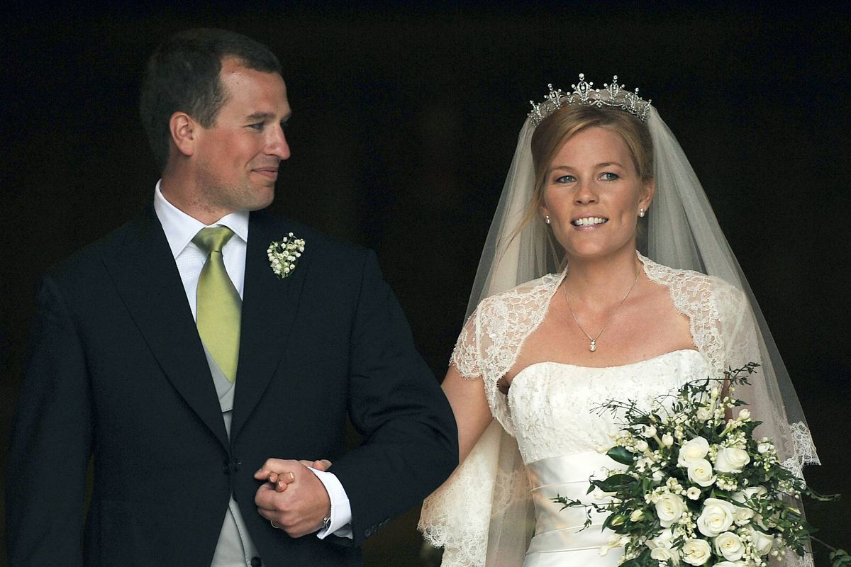 A newlywed couple, the groom in a formal suit and tie and the bride in a wedding gown with a bouquet of flowers, are walking side by side, possibly exiting a wedding venue.