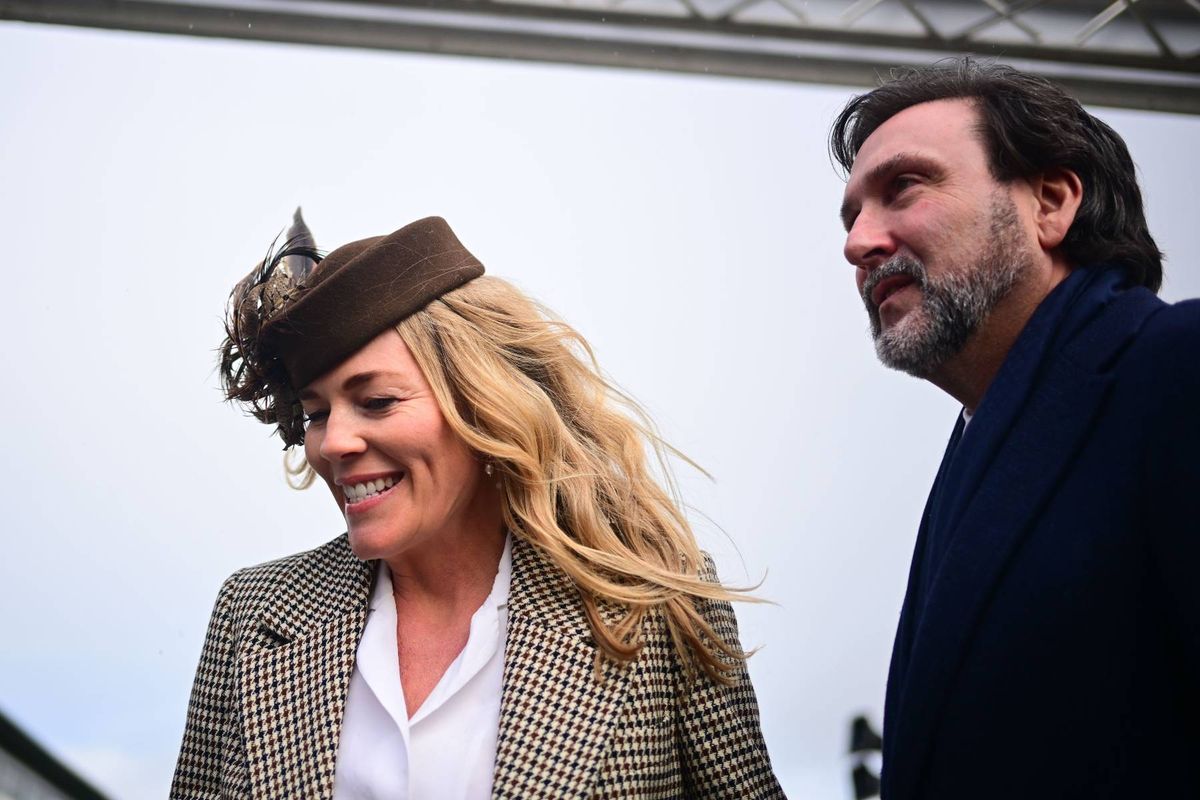 Two individuals, one wearing a hat and a coat, and the other dressed in a suit, standing next to each other and appearing to engage in conversation.
