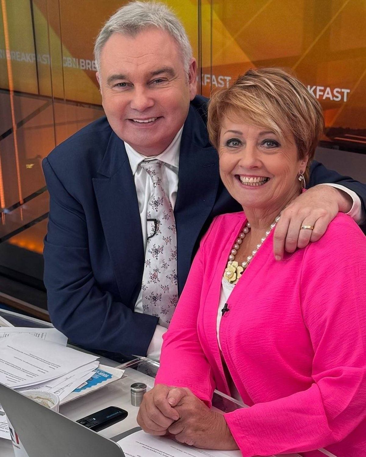 An adult male and female, dressed formally, are smiling and posing together for a photograph in a professional setting.
