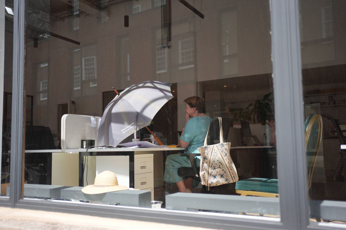 23/06/2026 - An office worker uses an umbrella to shade her workspace from the sun in Westminster, central London.