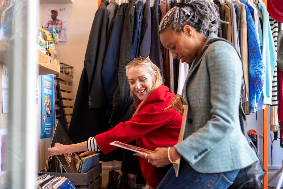 Women shopping in a thrift store in London's vibrant Shoreditch area have fun looking through a collection of vinyl records