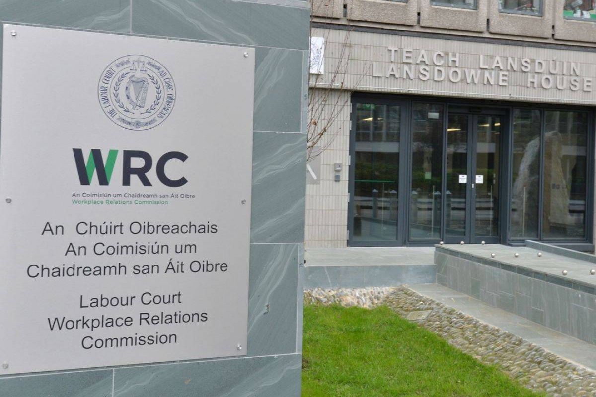 An outdoor signboard with the letters "WRC" prominently displayed is situated in front of a building with glass windows and a door. The sign includes additional text in a smaller font, although the specific content of the text is not discernible in this image. The area surrounding the sign features a neatly trimmed lawn.