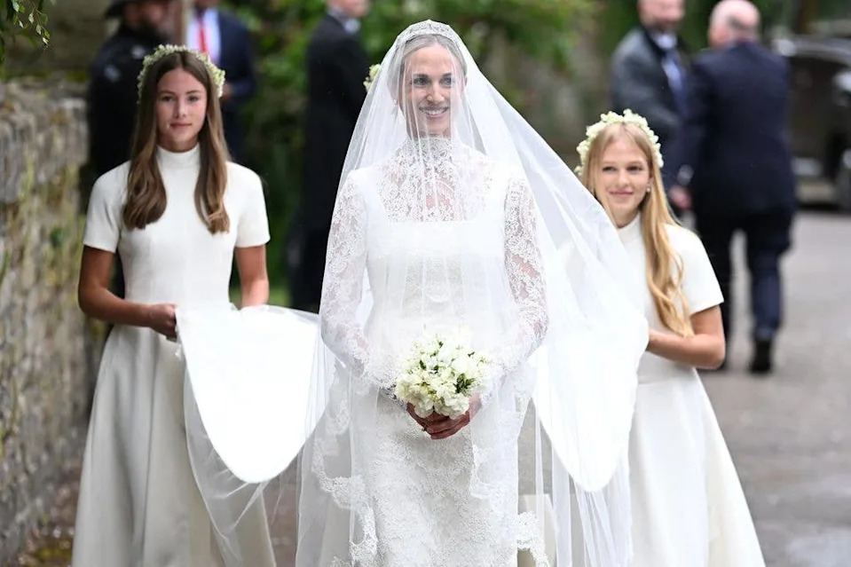 Harriet Sperling smiling wearing a white bridal gown with her three bridesmaids behind her