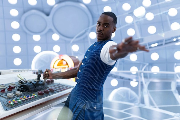 BBC-annual-report-2026 Ncuti Gatwa as Doctor Who stood in the Tardis one hand on the controls the other outstretched and wearing a determined look.