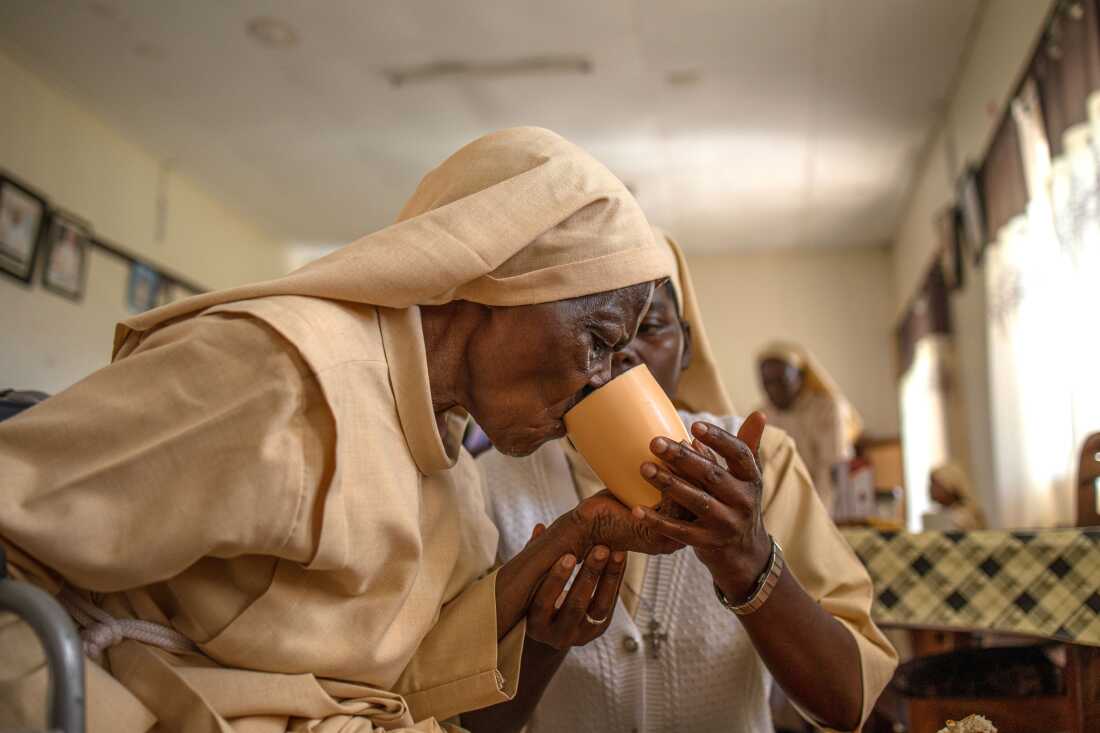 Sister Mary Consolata Nakawooja assists an elderly nun as she takes tea at the Little Sisters of St. Francis premises in Nkokonjeru, Uganda.