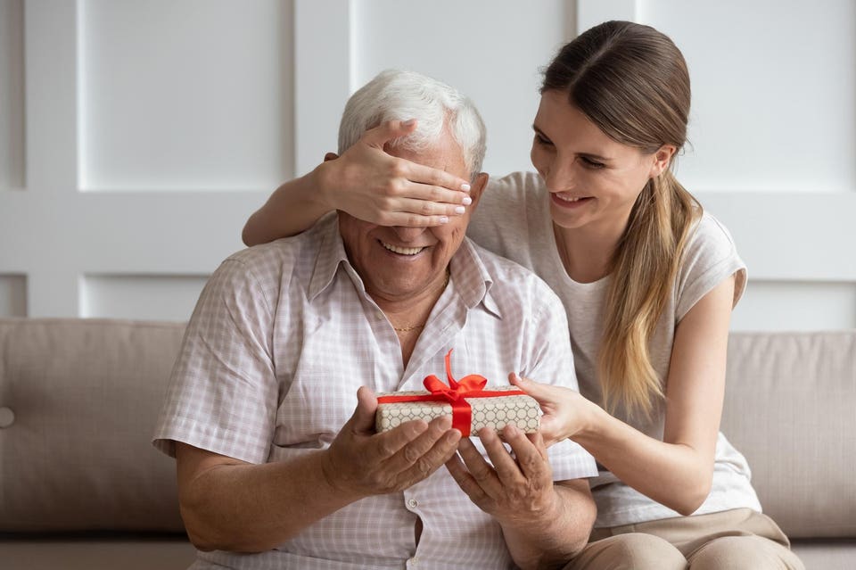 Smiling adult daughter closing older father eyes, preparing surprise