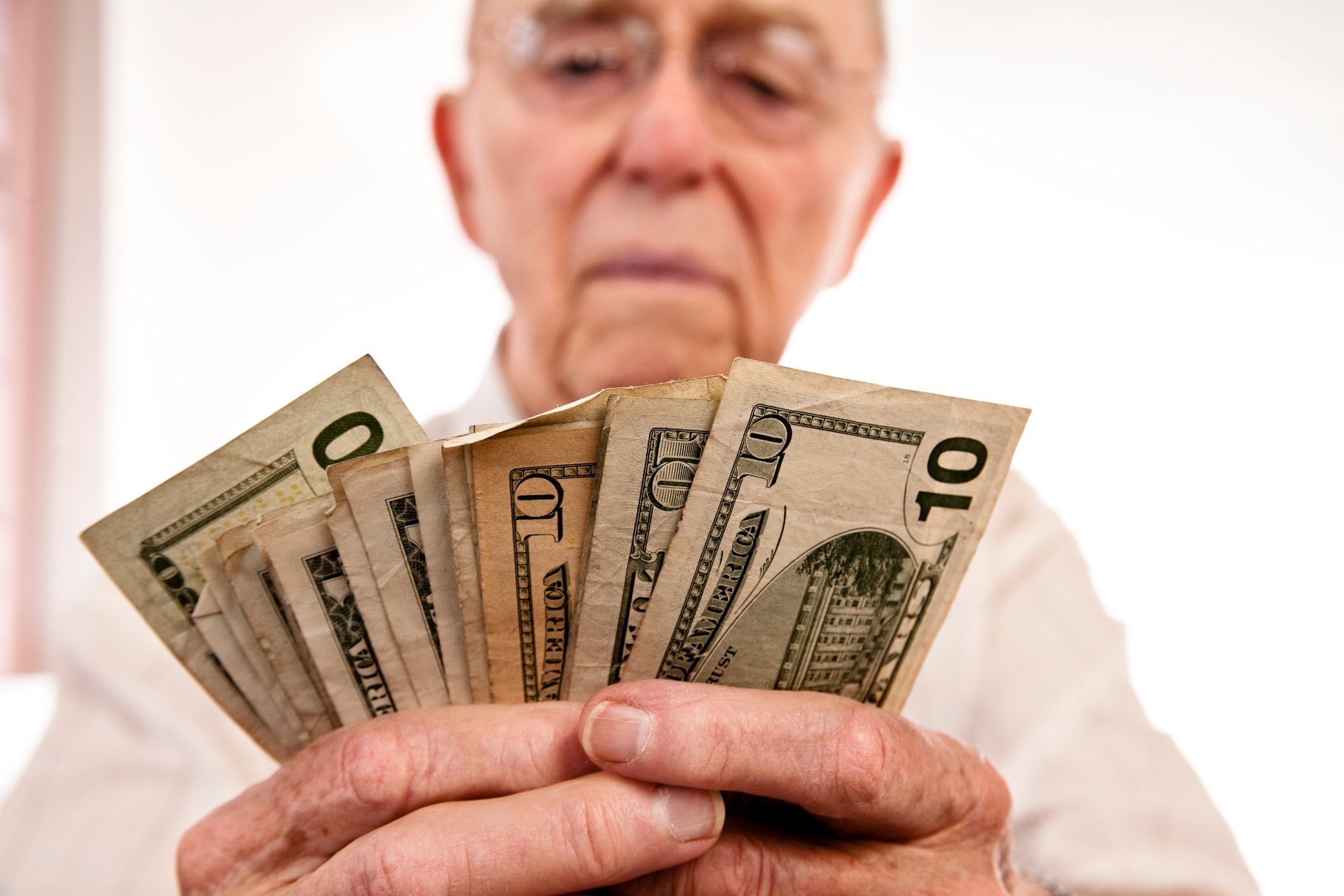 A seated person counting a fanned assortment of cash bills held in their hands.