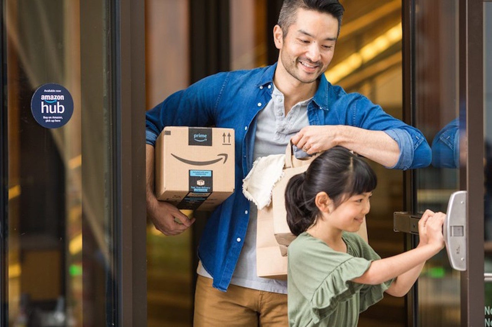 A parent holding an Amazon package while their child holds open a door for them.
