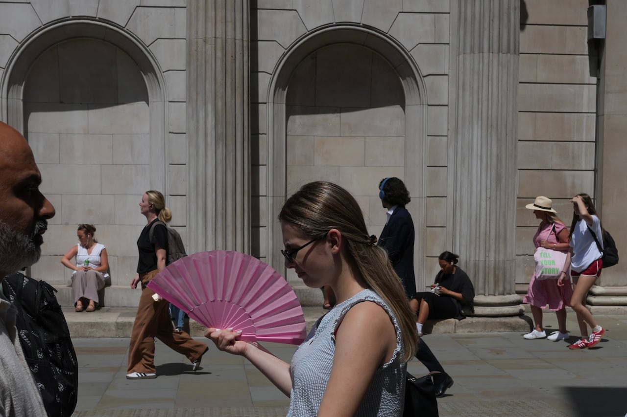 A woman cool herself with a fan on a hot day in London, England.