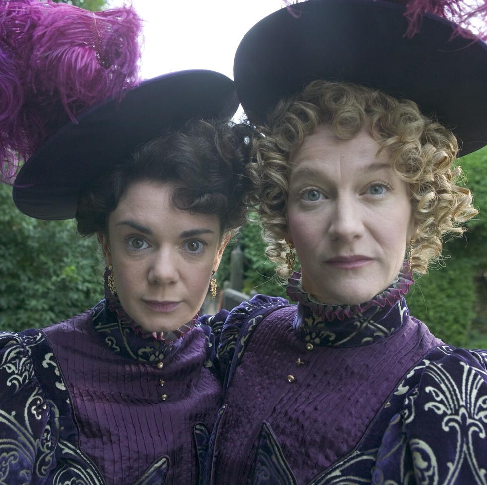 two individuals in elaborate purple costumes with large hats adorned with feathers