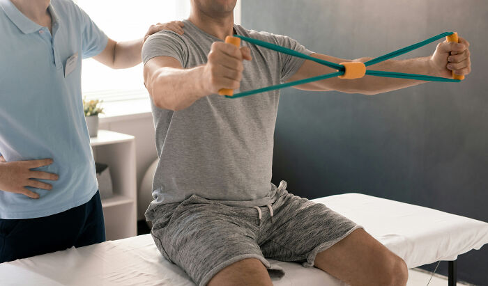 A nurse assists a patient with physical therapy, stretching with resistance bands to improve mobility.