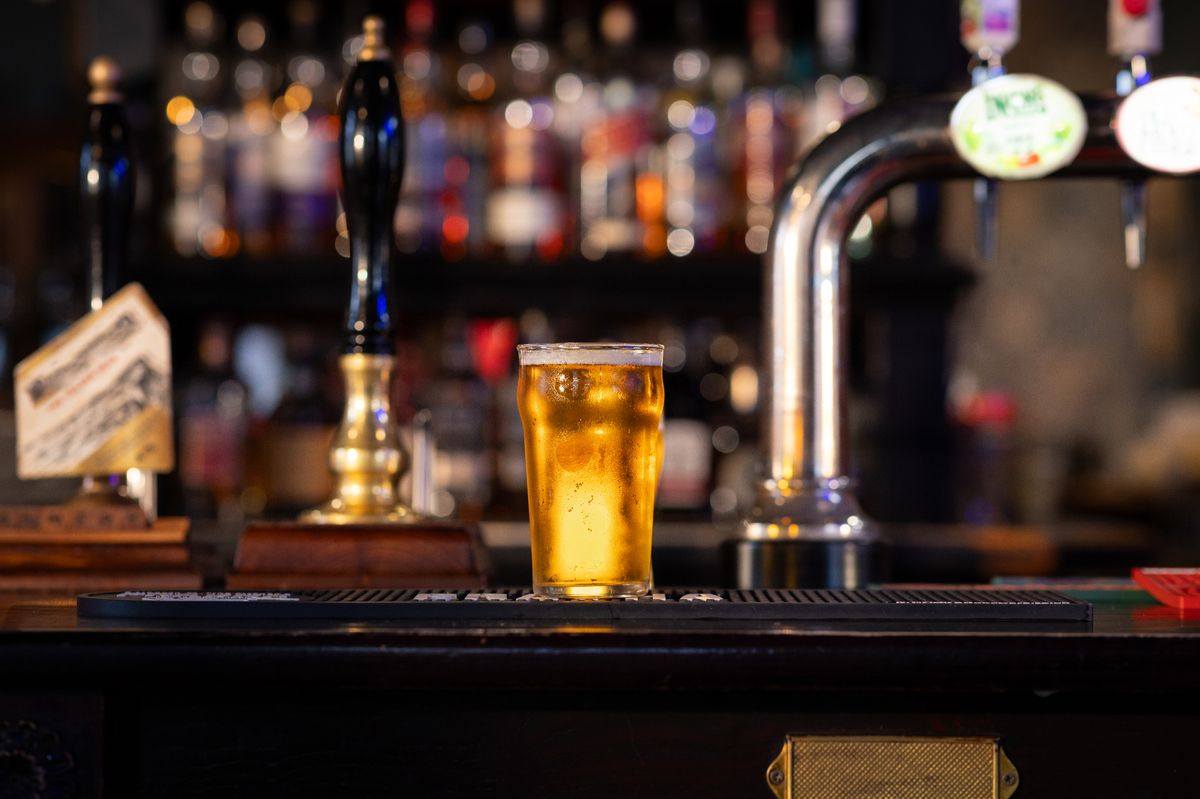 A full shot of a full pint of lager on a bar counter. The pint is overflowing with beer foam