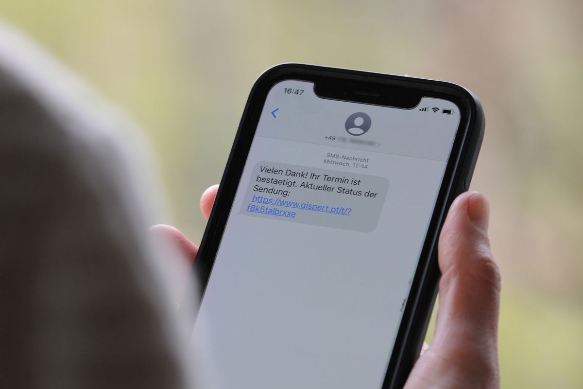 A woman holds a smartphone in her hand with a scam text message on the display.