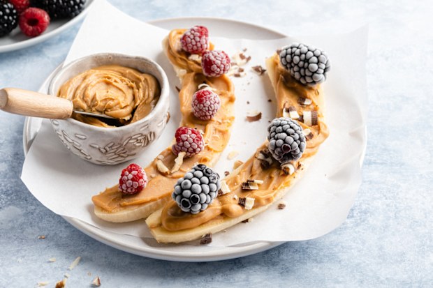 Banana with peanut butter spread on top and covered in frozen berries.