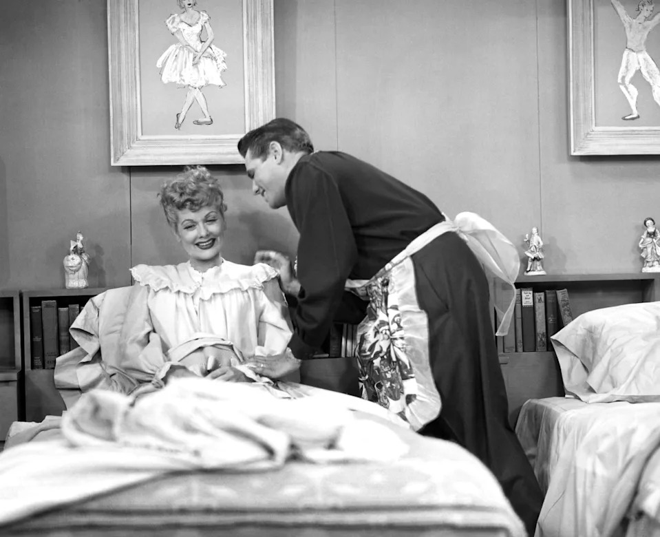 Lucy in bed and being kissed by Ricky, who is standing beside the bed