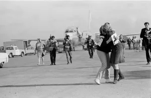Two excited fans hugging amidst photographers & cameramen recording The Beatles leaving SFO to Candlestick Park August 29, 1966