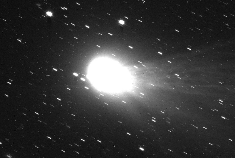 Large, bright white egg-shaped object. It has several diffuse filaments streaming behind it, and background stars.