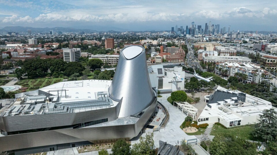 California Science Center in Los Angeles, a silver futuristic building beside low-rise buildings with a city skyline in the distance.