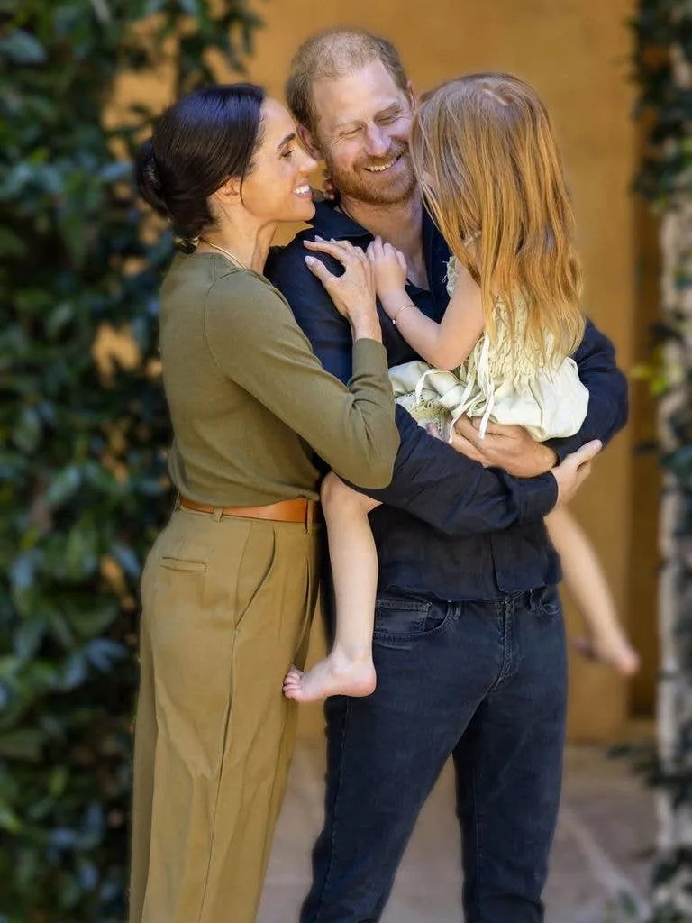 Prince Harry and Meghan, Duchess of Sussex, smiling and holding a young girl.