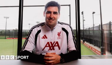 New Liverpool manager Andoni Iraola in white and black club training kit with red lettering, sitting at a table at the club's training ground